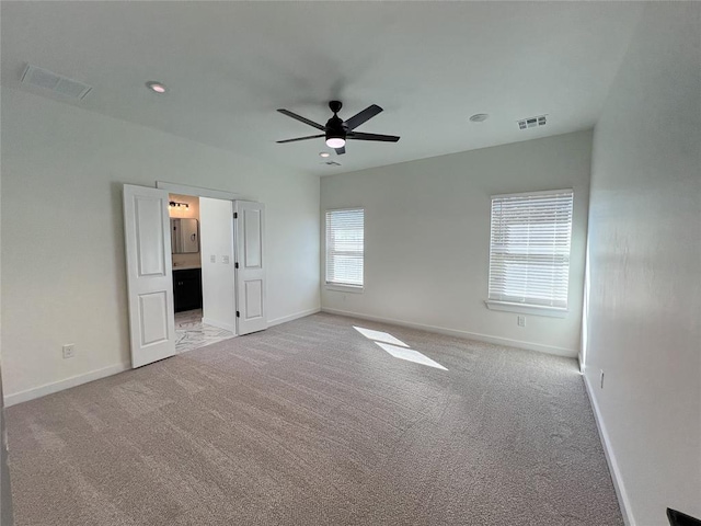 unfurnished bedroom with ceiling fan, light colored carpet, and ensuite bath