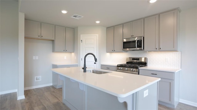 kitchen with a center island with sink, a kitchen breakfast bar, sink, light hardwood / wood-style floors, and stainless steel appliances