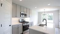 kitchen with gray cabinetry, an inviting chandelier, hanging light fixtures, sink, and appliances with stainless steel finishes