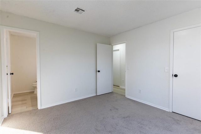 unfurnished bedroom featuring light colored carpet and connected bathroom