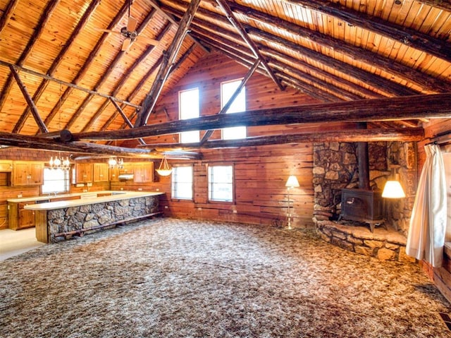 unfurnished living room featuring beam ceiling, a wood stove, wood walls, and wood ceiling