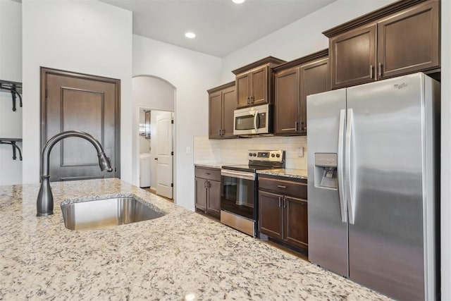 kitchen with light stone countertops, sink, tasteful backsplash, dark brown cabinets, and appliances with stainless steel finishes