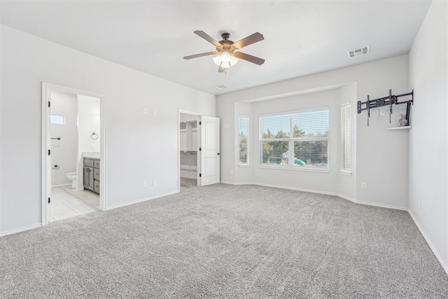 unfurnished bedroom featuring light carpet, a walk in closet, ensuite bathroom, ceiling fan, and a closet