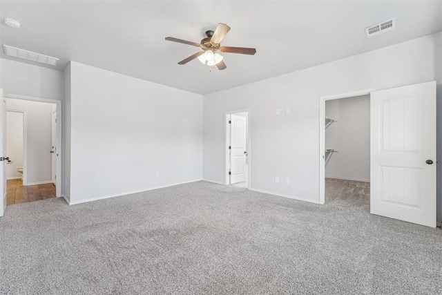 unfurnished bedroom featuring connected bathroom, ceiling fan, light colored carpet, a walk in closet, and a closet