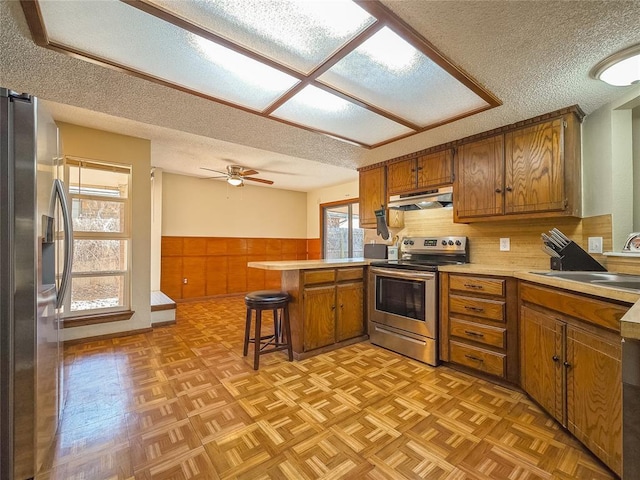 kitchen with kitchen peninsula, appliances with stainless steel finishes, sink, a kitchen bar, and a textured ceiling