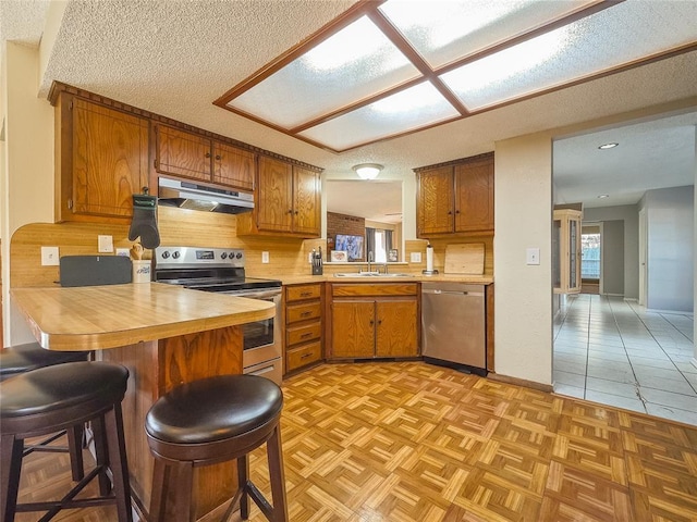 kitchen with a kitchen bar, appliances with stainless steel finishes, sink, kitchen peninsula, and light parquet flooring