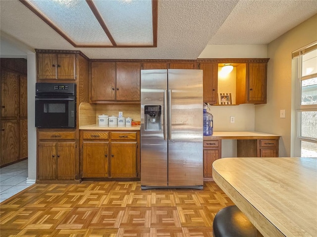 kitchen with light parquet floors, a textured ceiling, stainless steel fridge, and oven