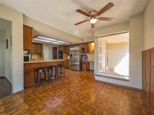 kitchen with a textured ceiling, stainless steel fridge with ice dispenser, kitchen peninsula, dark parquet flooring, and a breakfast bar area