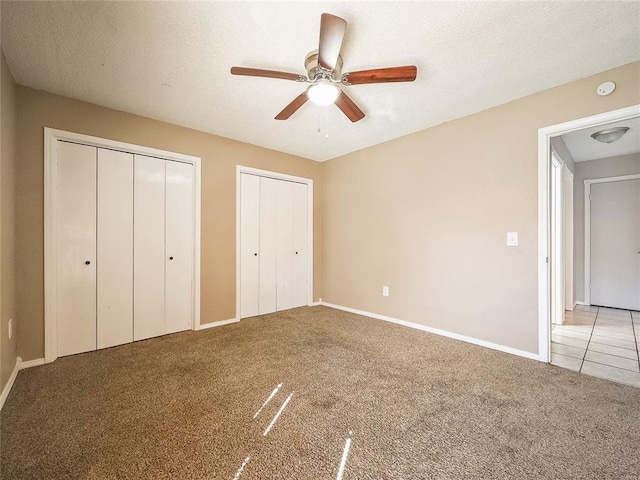 unfurnished bedroom with ceiling fan, a textured ceiling, light carpet, and two closets