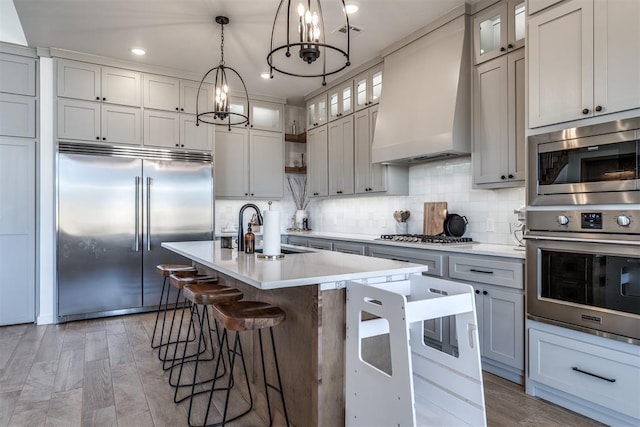 kitchen featuring sink, built in appliances, light hardwood / wood-style floors, a center island with sink, and custom exhaust hood