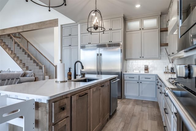 kitchen with decorative backsplash, sink, pendant lighting, light hardwood / wood-style floors, and an island with sink