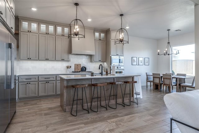 kitchen with sink, built in appliances, hanging light fixtures, and a kitchen island with sink