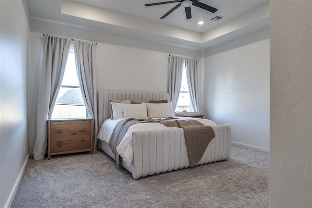 bedroom with ceiling fan, multiple windows, light carpet, and a tray ceiling