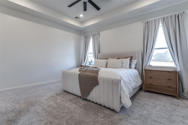 carpeted bedroom featuring a raised ceiling, multiple windows, and ceiling fan