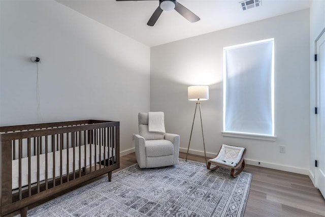 bedroom with ceiling fan, hardwood / wood-style floors, and a crib