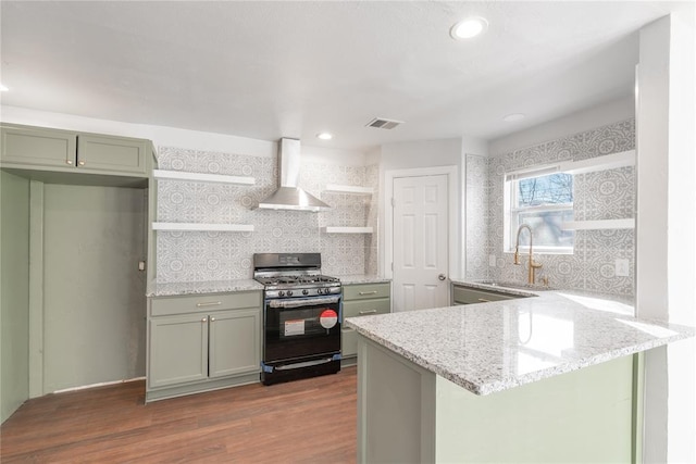 kitchen with sink, wall chimney range hood, black range with gas stovetop, light stone counters, and kitchen peninsula