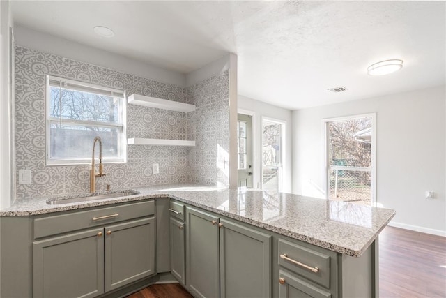 kitchen with light stone countertops, kitchen peninsula, sink, and tasteful backsplash