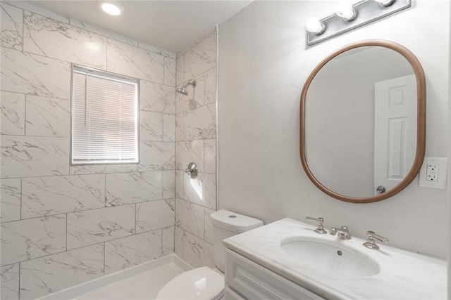 bathroom featuring a tile shower, vanity, and toilet