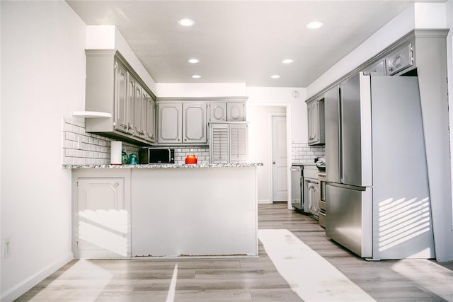 kitchen featuring gray cabinetry, light stone counters, kitchen peninsula, stainless steel fridge, and decorative backsplash