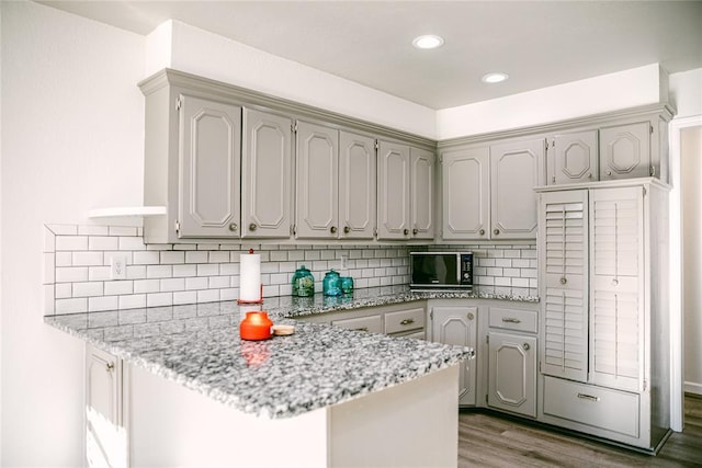 kitchen with gray cabinetry, backsplash, light wood-type flooring, light stone counters, and kitchen peninsula