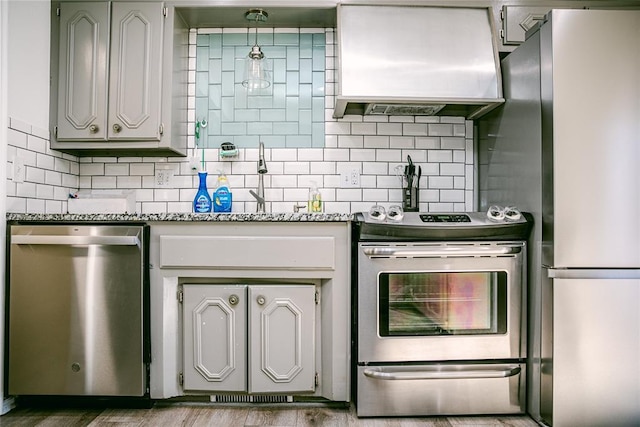 kitchen featuring ventilation hood, decorative backsplash, light wood-type flooring, light stone countertops, and appliances with stainless steel finishes