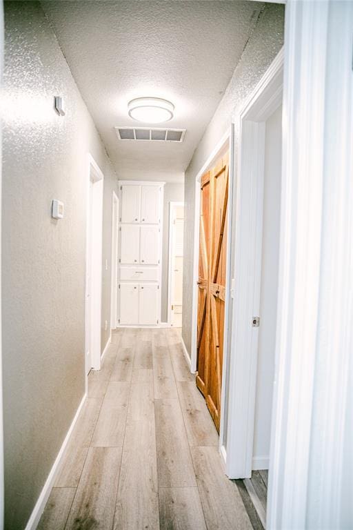 hall with light hardwood / wood-style flooring and a textured ceiling