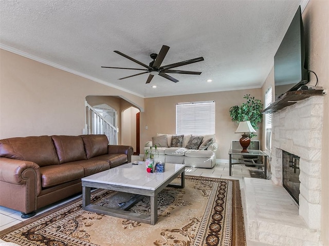 tiled living room featuring a fireplace, ceiling fan, crown molding, and a textured ceiling