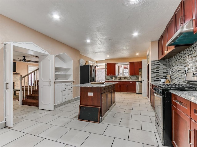 kitchen with backsplash, light stone counters, stainless steel appliances, ceiling fan, and a center island