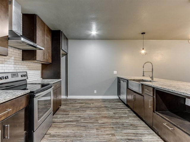 kitchen with sink, wall chimney exhaust hood, appliances with stainless steel finishes, decorative light fixtures, and light stone counters