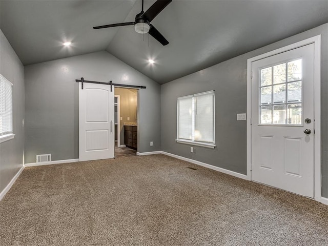 interior space with connected bathroom, ceiling fan, a barn door, carpet floors, and lofted ceiling