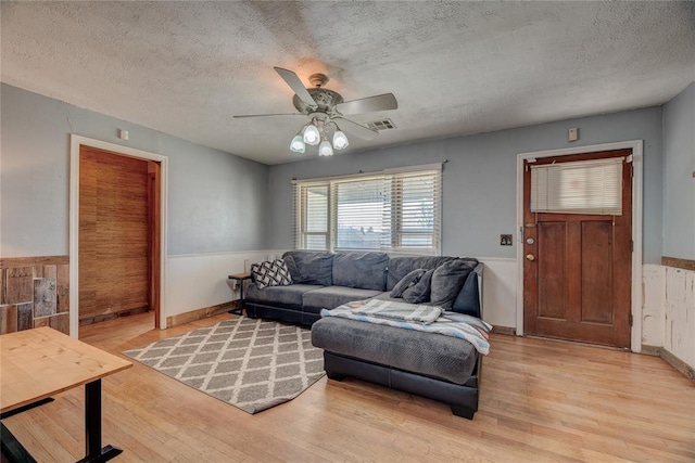 living room with a textured ceiling, light hardwood / wood-style flooring, ceiling fan, and wood walls