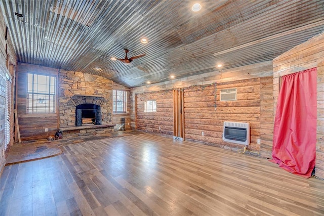 unfurnished living room featuring heating unit, vaulted ceiling, ceiling fan, wooden walls, and a fireplace