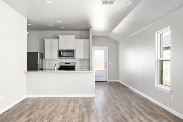 kitchen with backsplash, light stone counters, stainless steel appliances, white cabinetry, and lofted ceiling