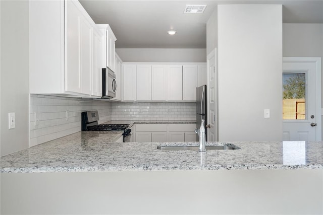 kitchen featuring sink, stainless steel appliances, light stone counters, decorative backsplash, and white cabinets