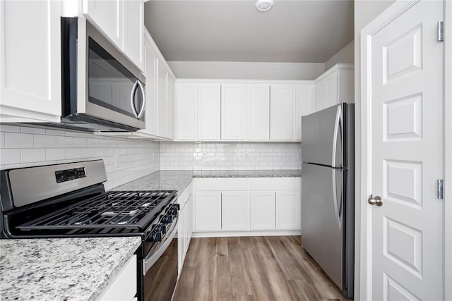 kitchen featuring light stone countertops, white cabinets, stainless steel appliances, and light hardwood / wood-style floors