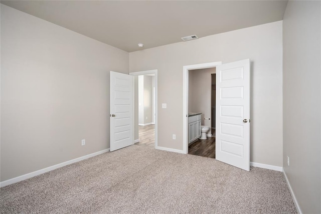 unfurnished bedroom featuring ensuite bathroom and dark carpet