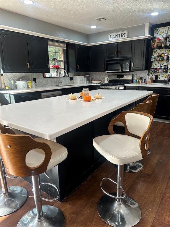 kitchen with a kitchen breakfast bar, sink, a textured ceiling, and stainless steel range