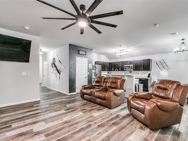 living room featuring ceiling fan with notable chandelier, light wood-type flooring, lofted ceiling, and sink