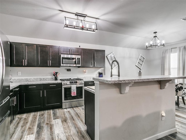 kitchen featuring a kitchen bar, stainless steel appliances, a kitchen island with sink, pendant lighting, and a chandelier