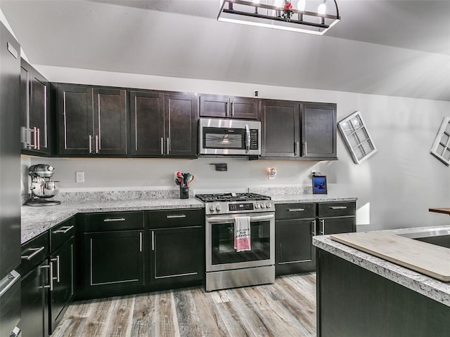 kitchen with dark brown cabinetry, light stone counters, light wood-type flooring, and appliances with stainless steel finishes