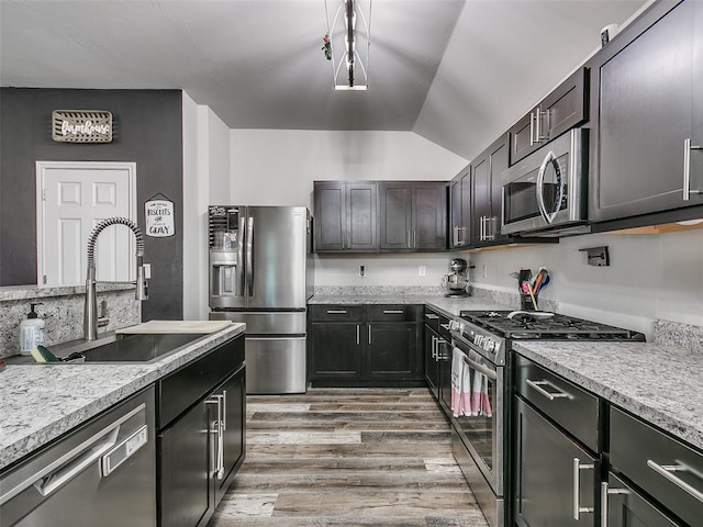 kitchen featuring appliances with stainless steel finishes, dark brown cabinets, sink, decorative light fixtures, and hardwood / wood-style flooring