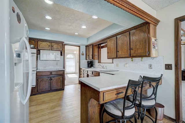 kitchen featuring tasteful backsplash, a kitchen breakfast bar, kitchen peninsula, white appliances, and light hardwood / wood-style flooring