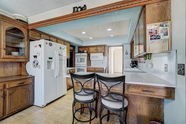 kitchen with sink, white appliances, a breakfast bar, a textured ceiling, and light wood-type flooring