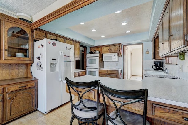 kitchen featuring sink, white appliances, light hardwood / wood-style floors, a textured ceiling, and kitchen peninsula