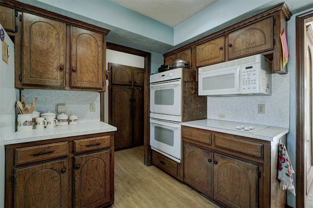 kitchen with dark brown cabinetry, white appliances, and light hardwood / wood-style floors