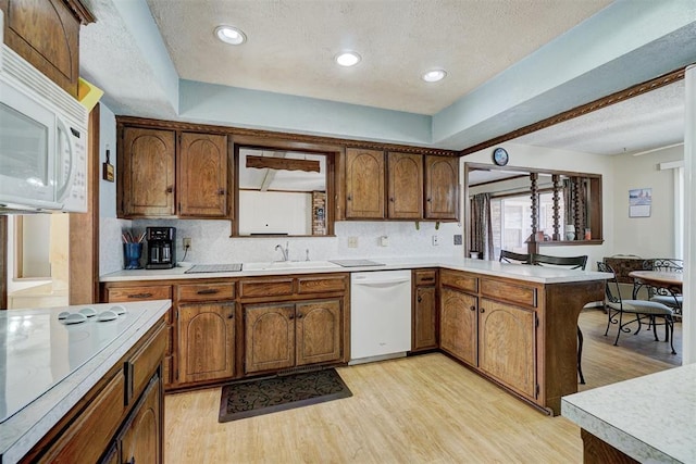 kitchen with sink, tasteful backsplash, light hardwood / wood-style flooring, kitchen peninsula, and white appliances