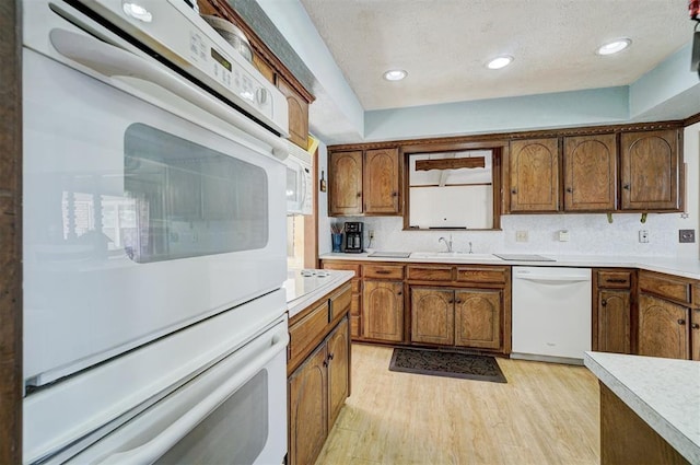 kitchen featuring sink, white appliances, a textured ceiling, and light wood-type flooring