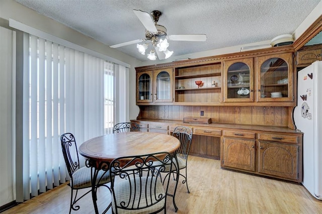 dining space with a textured ceiling, ceiling fan, and light hardwood / wood-style flooring