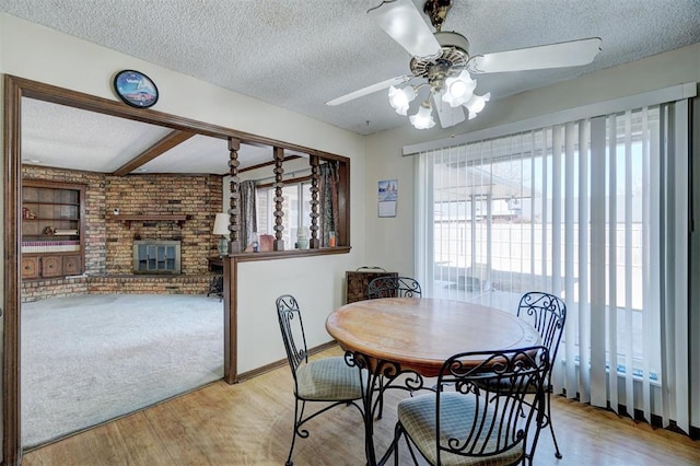 dining area with ceiling fan, a fireplace, light hardwood / wood-style floors, and a textured ceiling