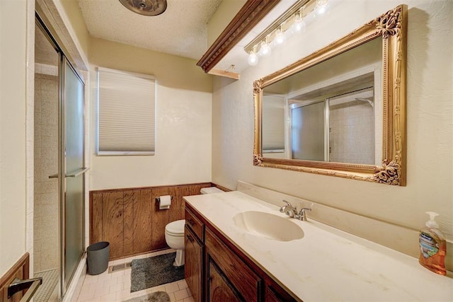 bathroom featuring wooden walls, vanity, toilet, a shower with door, and a textured ceiling